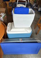 Photo showing stacked coolers and a large plastic storage tote in a garage setting.