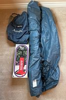 Photo shows the rolled-up blue AeroBed inflatable mattress with attached black cord, a blue AeroBed carrying bag, and a boxed manual air pump.