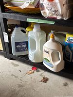 Photo showing three large plastic jugs comprising Allen's clear jug, ECOS and Kirkland laundry detergent, located on a shelf in garage.