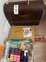 Vintage Singer sewing machine in dark wooden case with key, a box labeled knitting, and a container with colorful yarn skeins and sewing supplies.
