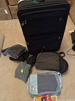 Large black suitcase, multiple bags, compression cubes, neck pillow, and packing accessories arranged on carpet