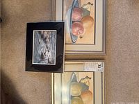 Two framed watercolour paintings featuring fruit still life and one smaller unframed watercolour painting of rocky shoreline
