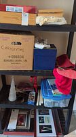 Shelf containing various Christmas decorations in boxes, bins, a stocking, picture frames, and a clear cone decoration