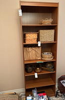 Full bookshelf showing five shelves with various wicker baskets and small decorative bowls, used condition obvious from surface wear.