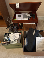 Top angled view of the wooden music center with open lid showing turntable and accompanying boxes with CDs, manuals, and accessories.