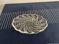 Large glass platter with swirling raised petal design on top of dark cloth with white zigzag pattern