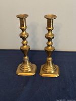 Pair of polished brass candlesticks with decorative bases and smooth finish on a dark cloth background