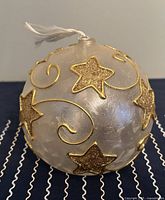 Photo of the glass Christmas ball ornament with gold glitter stars and swirls, showing the ornament's decorative details.