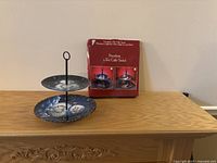 Porcelain two-tier cake stand with snowman winter design on navy blue plates, along with its box showing the product image.