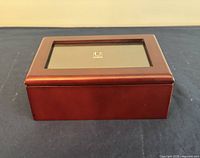 Closed rectangular wooden jewelry box with a reddish-brown finish and photo frame on top, set on a dark blue surface.