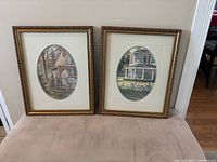 Two framed Trisha Romance pictures with gold-tone frames and white mats, showing quaint cottage scenes in Barnard Castle, England.