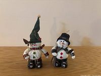 Two plush snowman figurines in skiing attire with ski poles on a wooden surface.