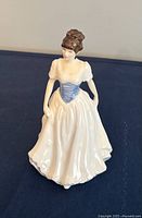 Royal Doulton porcelain figurine of woman in white dress with blue corset on blue surface.