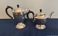 Front view of silver coffee pot and teapot with black handles on dark surface.
