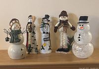 Five snowman figurines arranged on shelf showing variety of styles and materials