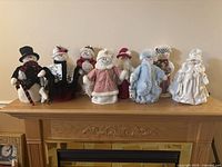 Eight snowlady plush decorations lined up on a mantel, each with distinct winter outfit, hats, and accessories.