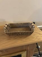 Rectangular woven basket with wooden handles on wooden table, neutral background