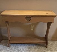 Front view of small pine table with heart cutout on apron and bottom shelf.