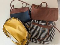 Three bags placed flat on surface: Madden Girl yellow backpack, Esprit navy and brown small purse, Reitmans yellow purse.
