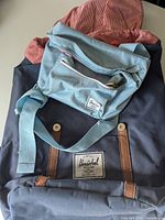 Photo showing both the Herschel dark blue backpack with brown straps and light blue crossbody bag with adjustable strap.