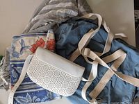 Photo showing white perforated belt bag, three scarves in blue, red floral and abstract gray patterns, and blue canvas weekend bag with cream straps partly visible