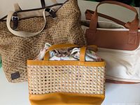 Three bags, including woven tote, yellow Love & Lore weekender bag with colorful bead embellishments, and large Toms bag with brown handles