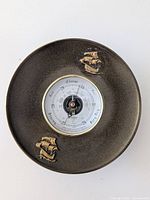 Front view of circular barometer with two brass ship figures and white dial with weather markings.