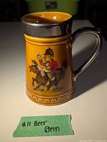 Side view of ceramic beer stein showing mounted soldier figure in red jacket with raised beer mug, mustard-yellow body, and dark glazed handle and rim.