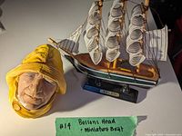 Bossons head fisherman sculpture with accompanying miniature model sailboat on a flat surface, showing the overall lot
