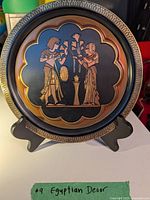 Front view of the round decorative plate depicting two ancient Egyptian figures holding lotus flowers, showing detailed design and color.