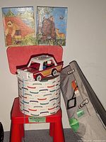 Red Ikea kid's chair with fabric storage bin and Fisher-Price toy car on top, along with a lamp shade leaning to the side.