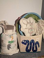 Photo of storage bin with a blue snake design, three animal-shaped cushions featuring a deer, mouse, and owl, and a cylindrical forest animal patterned sleeping bag or cushion.