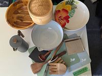 Overview photo showing the wooden salad bowl, bamboo steamer, ceramic bowls, wooden utensils, silicone mats, French press, and dough cutter, giving a full view of the lot.
