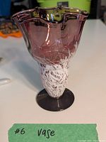 Full view of the glass vase showing purple glass body and white patterned base on a black foot.