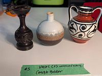 Three items on table: dark wooden candle holder, small round pottery vase with white and brown glaze, and double-handled Ukrainian pottery vase with red, white, and black decorative patterns.