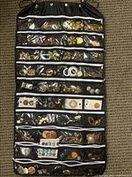 Full view of black hanging organizer with top-to-bottom clear zippered pockets filled with assorted buttons including metallic gold, silver, and decorative styles.