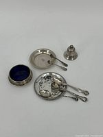 Overview of all sterling silver items including bell, salt cellar, glass liner, spoon rest with spoons, beaded dish and small spoons