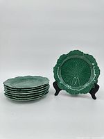 Group of eight green leaf shaped Wedgwood Majolica plates stacked with one displayed on stand showing front leaf detail.