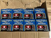 Wide view of eight unopened Rawlings Official Softball boxes in a cardboard box.