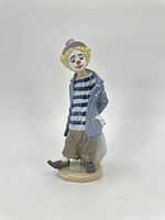 Front view of Lladro clown figurine wearing blue coat, striped shirt, and holding knapsack