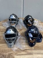 Four Pro Nine catcher's helmets arranged on wooden surface, two silver and two navy.
