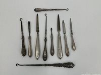 View of nine antique or vintage button hooks and small tools lying flat, showing variety of handle designs and hook/blade shaped tips