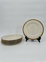 Set of six cream colored Lenox Lowell plates with gold rims, stacked and one on a stand facing forward showing detailing