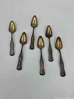 Set of six vintage melon spoons with gold-tone melon bowls and silver patterned handles, arranged on white background.