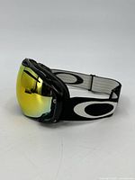 Side angle view showing black frame, yellow mirrored curved lens, and black elastic strap with large white Oakley logo.