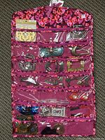 Pink floral fabric jewelry organizer with multiple clear pockets showing various metal belt buckles and accessories inside.
