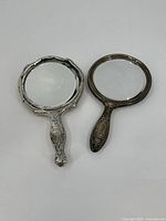 Two sterling silver weighted hand mirrors lying flat with glass facing upward, showing front reflective surfaces and metal frames