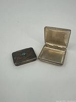 Two small rectangular silver pillboxes, one open and one closed, showing interior and exterior.