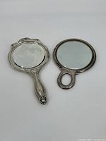 Top view of two vintage hand mirrors showing reflective glass and ornate handles.