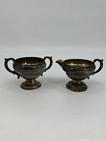 Pair of weighted sterling silver cream and sugar set on pedestal bases with ornate handles.